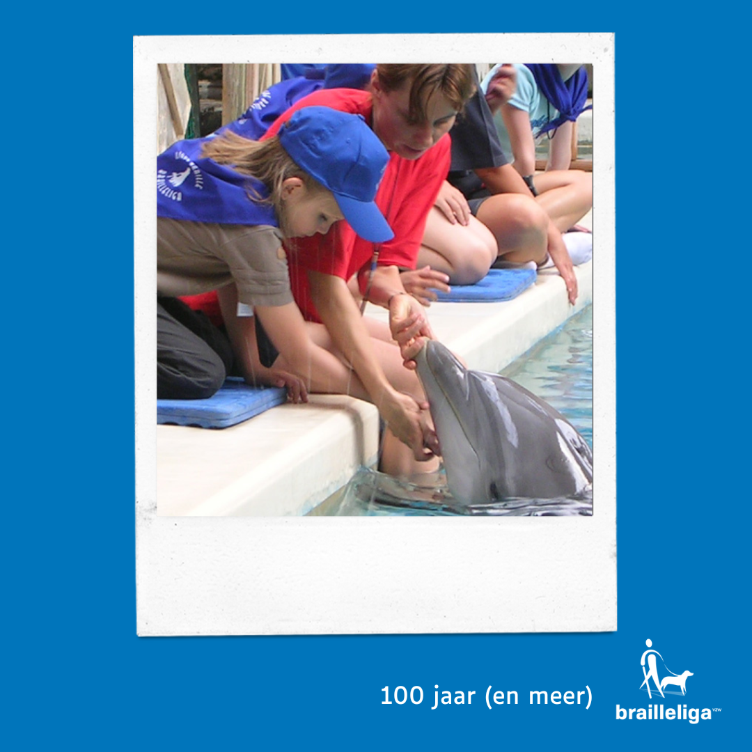 Foto van een blind kindje dat een dolfijn aait in het Boudewijn SeaPark, tijdens de BrailleDay in 2003.  